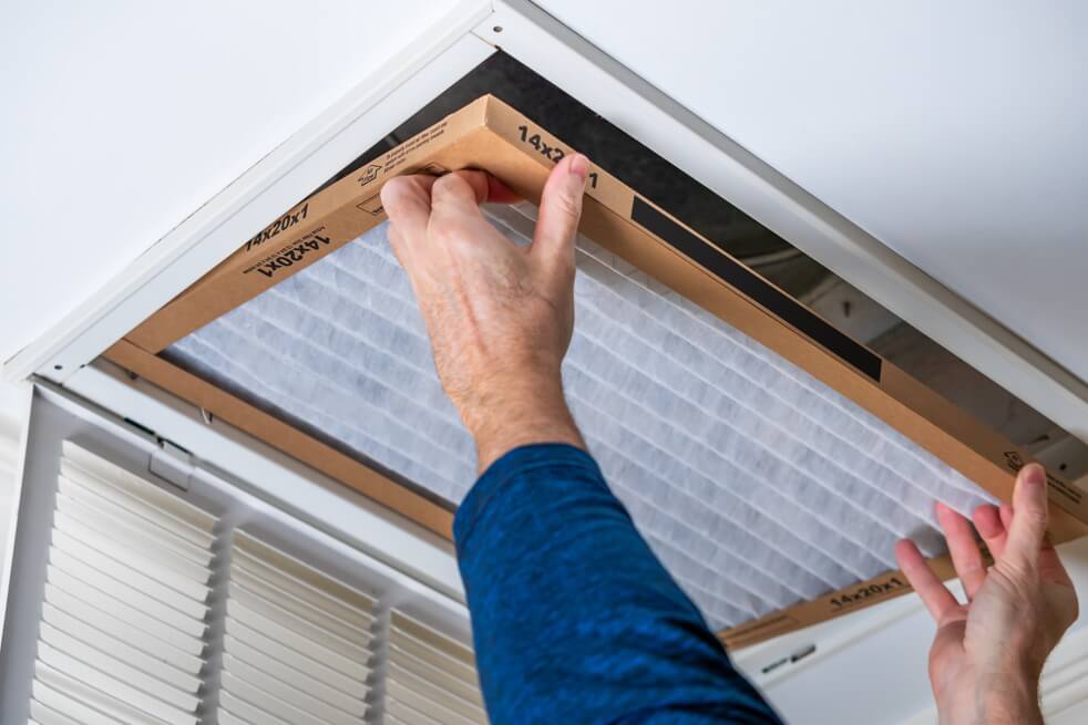 Man replacing dirty HVAC air filter in ceiling vent