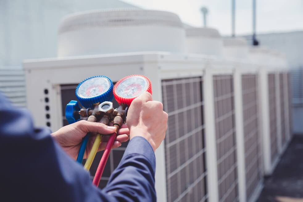 technician with gauges standing in front of HVAC units