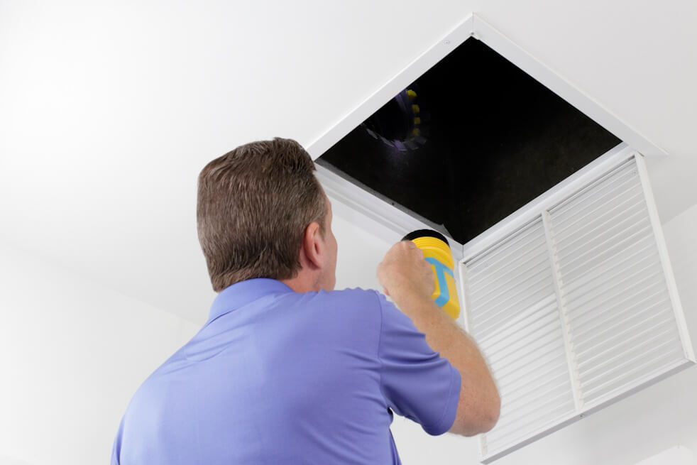 man with a flashlight looking up into an open air vent