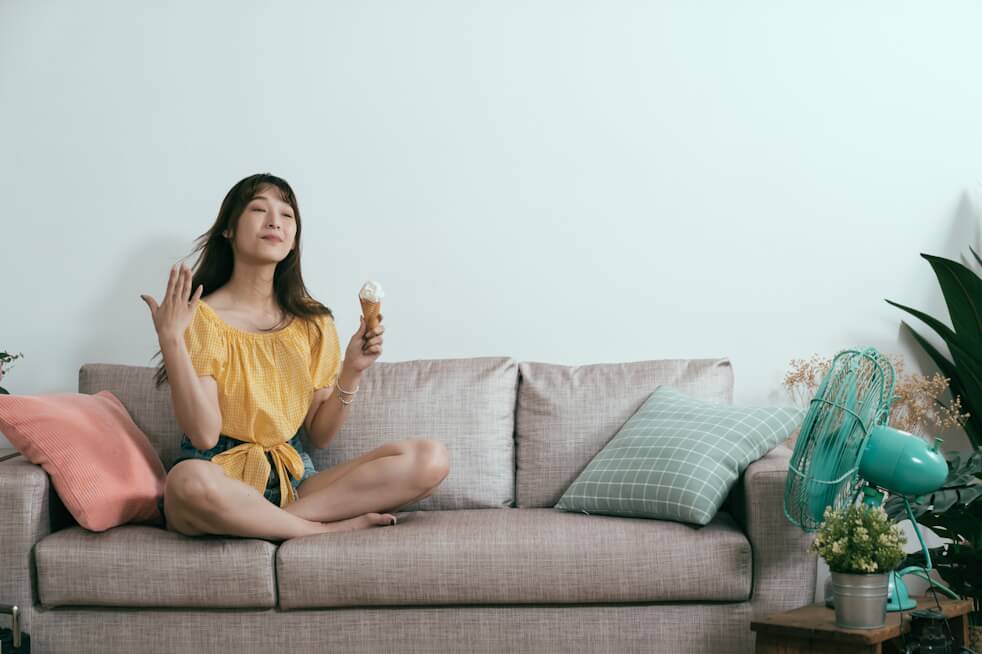 woman sitting on couch with fan blowing on her