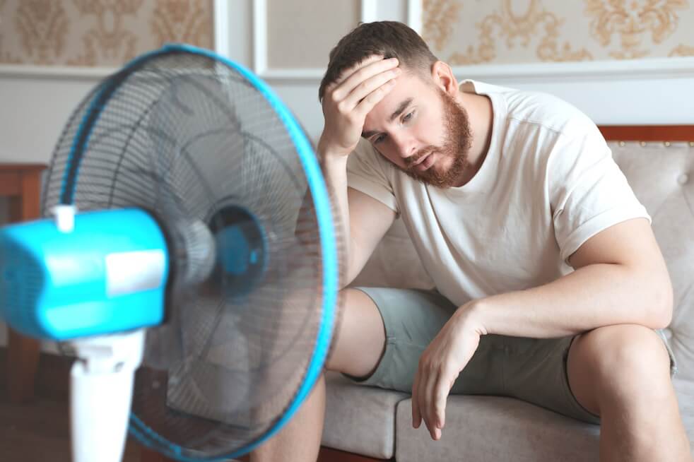 man sitting in front of fan in hot house